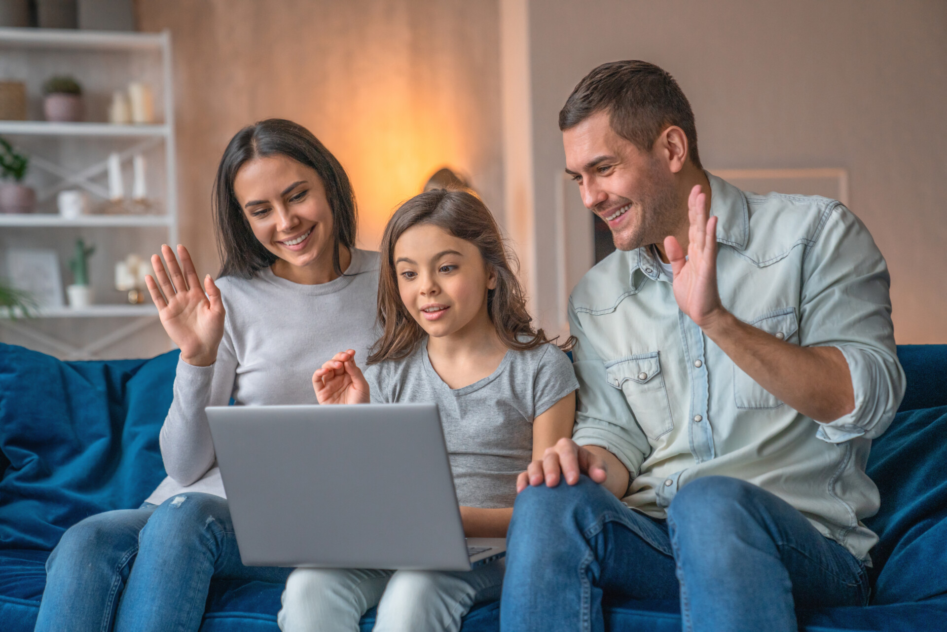 Happy family waving hands looking at web camera using laptop for video call, smiling