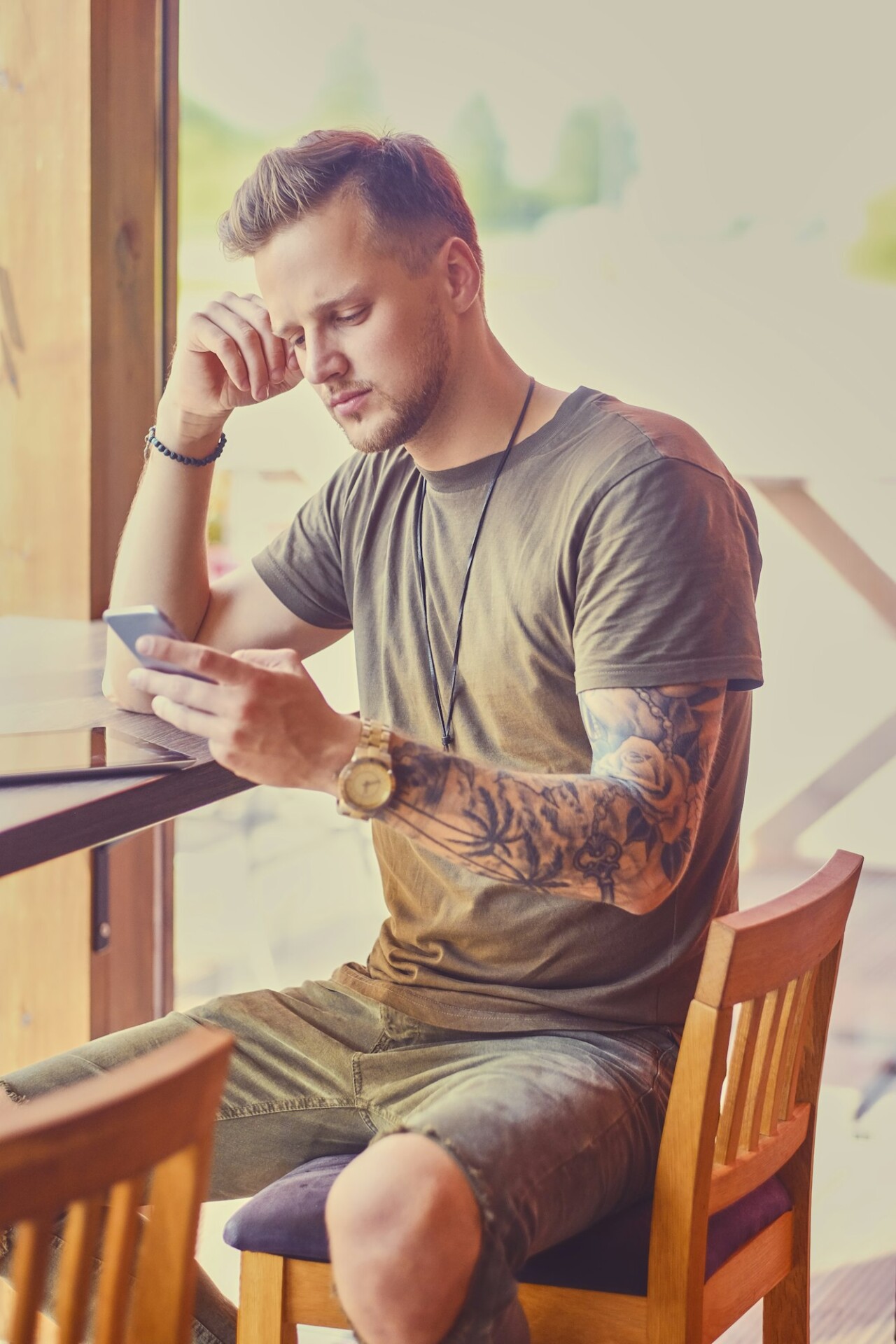 A man using smartphone in a cafe near window.