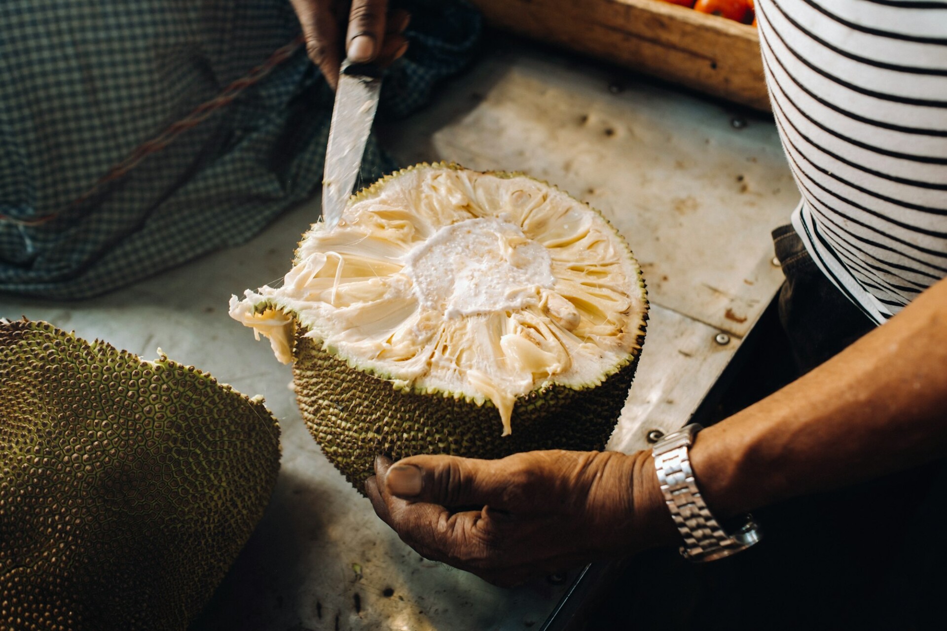 The seller cuts a juicy, ripe jackfruit for tourists. The urban market of Port Louis, Mauritius