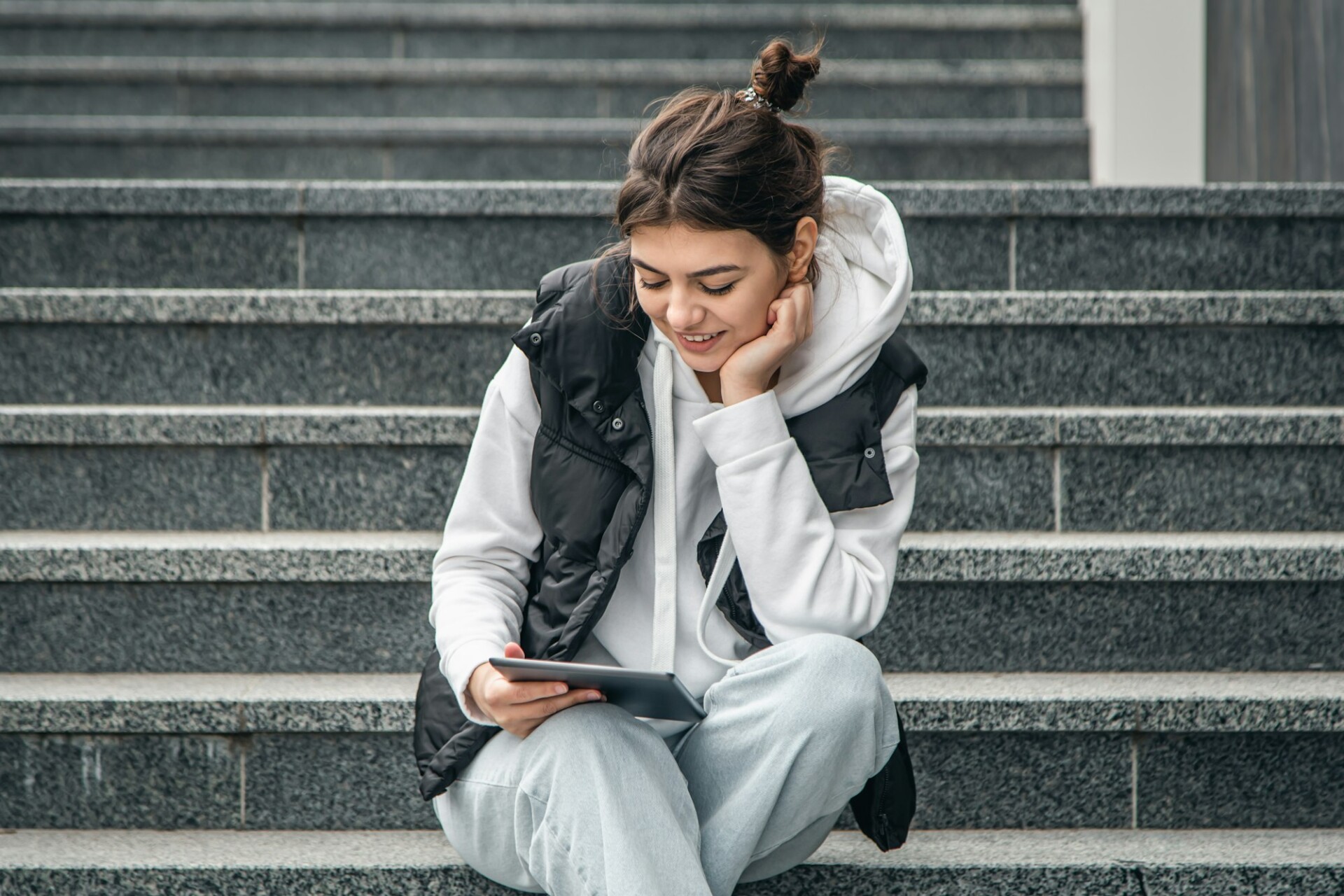 A young female student stands with a digital tablet in her hands outside.