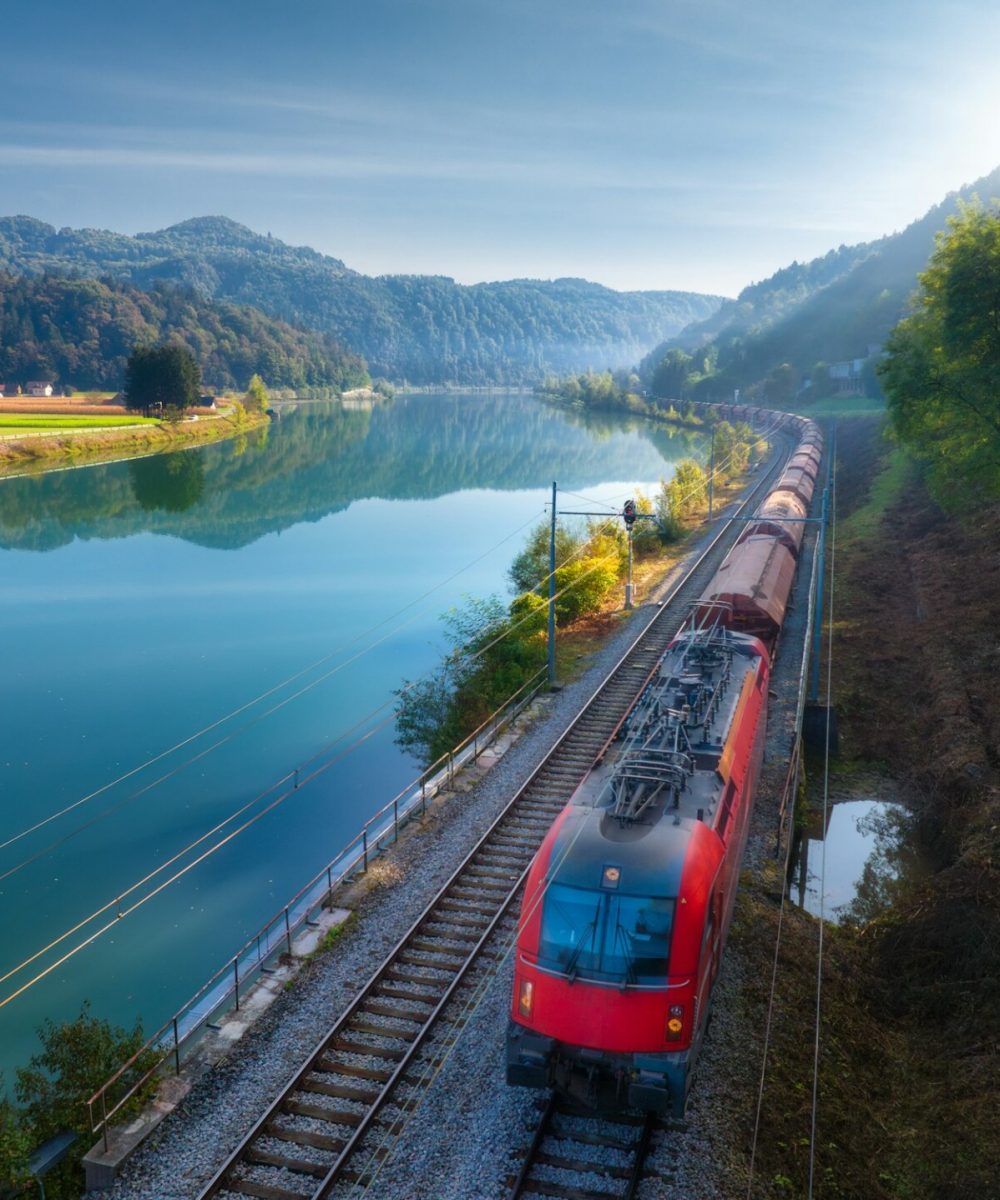 Aerial view of red speed train moving near river in mountains