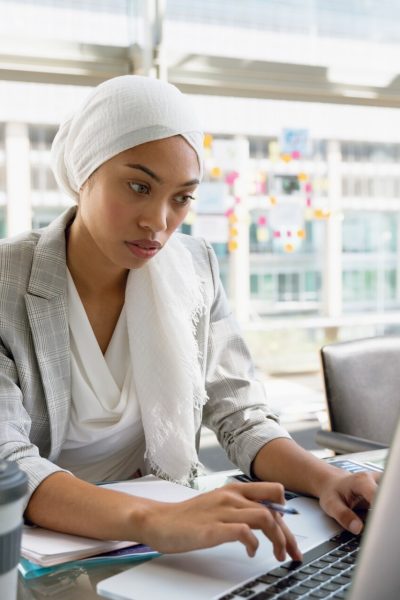 Businesswoman in hijab working on laptop at desk in a modern office