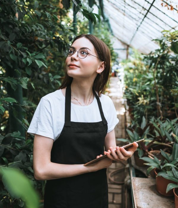 Young woman gardener in glasses and apron with digital tablet working in a garden center